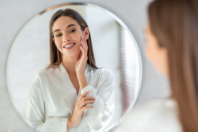Žena nanosi kremu na lice gledajući se u ogledalu